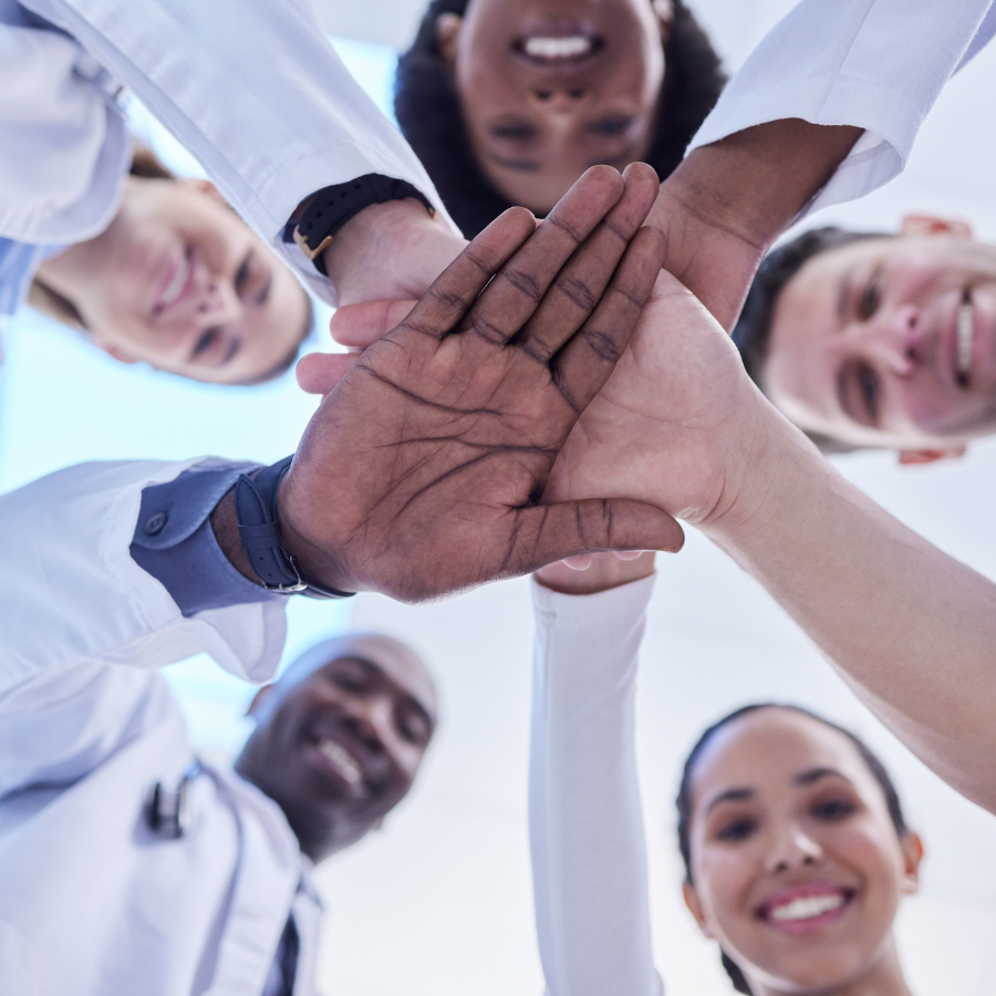 Healthcare, teamwork and hands together in huddle for team building, collaboration and motivation at hospital. Doctors, happy faces of medical employees in solidarity and help or support from below.