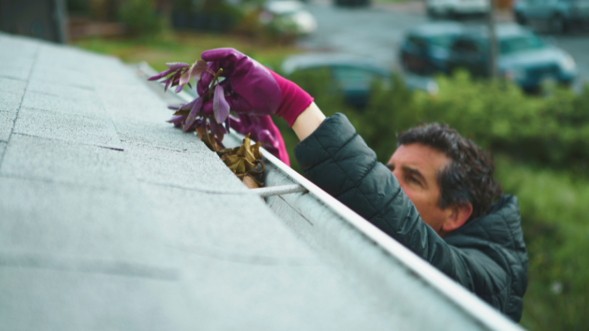 A man reaching up and cleaning gutters on a house.
