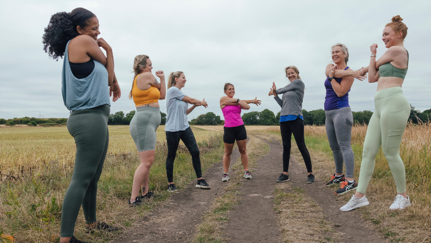 A shot of a group of diverse female friends outdoors on a field. They are stretching and preparing for a run.