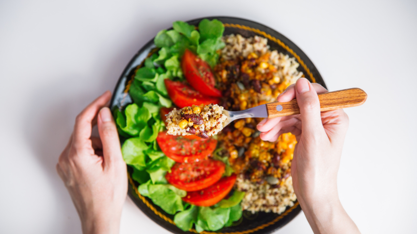 Two hands holding a bowl with a gluten-free meal made with quinoa, spinach and vegetables.