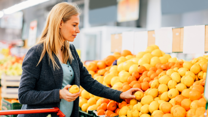 Pregnant woman shopping in a supermarket. Choosing fruits and putting them in a shopping cart. 
