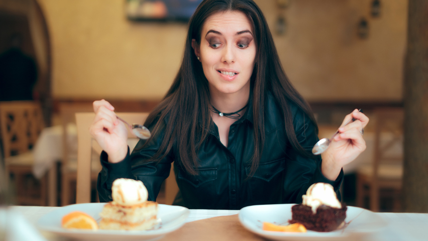 A young woman sits at a table in a restaurant with two pieces in front of her. She is trying to decide what pie to have, lemon or chocolate.