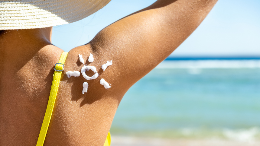 Back view of a young woman tanning at the beach with sunscreen cream in a sun shape on her shoulder. Wear sunscreen for skin cancer prevention!