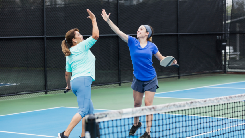 Latino mom and daughter high fiving on the pickleball court. 