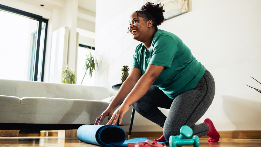 Young mixed-race woman exercising at home while smiling because she knows what to expect after her bariatric surgery.