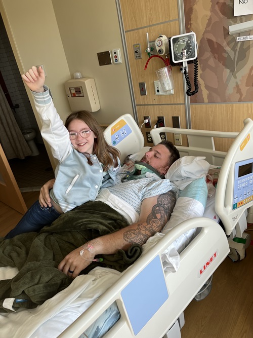 Samuel Neelands, Danbury Hospital spine surgery patient, in a hospital bed. His daughter is lying with him.