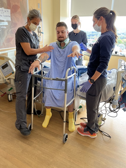 Samuel Neelands, Danbury Hospital spine surgery patient, using a walker to stand up off the hospital bed. A Danbury Hospital rehabilitation team is helping him stand up.