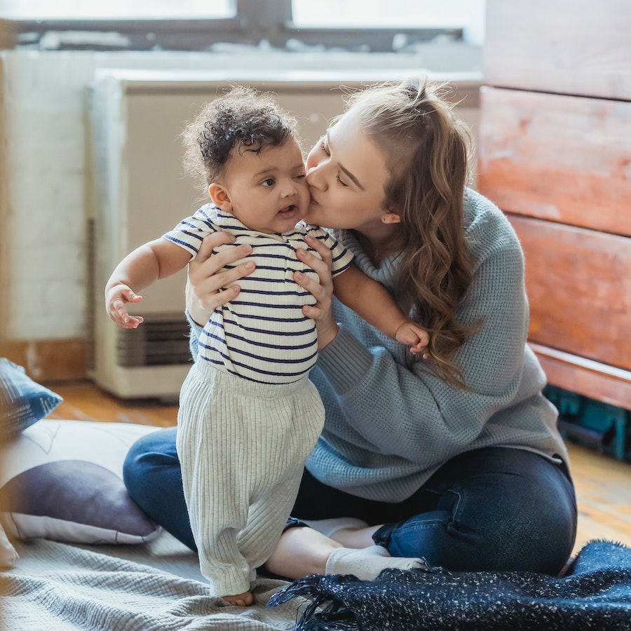 Loving mother kissing baby while sitting on the floor