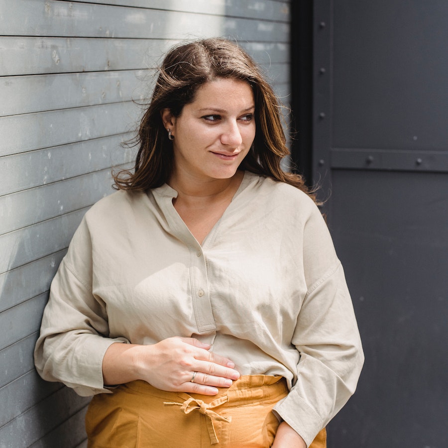 Pregnant woman in yellow pants smiling and holding stomach